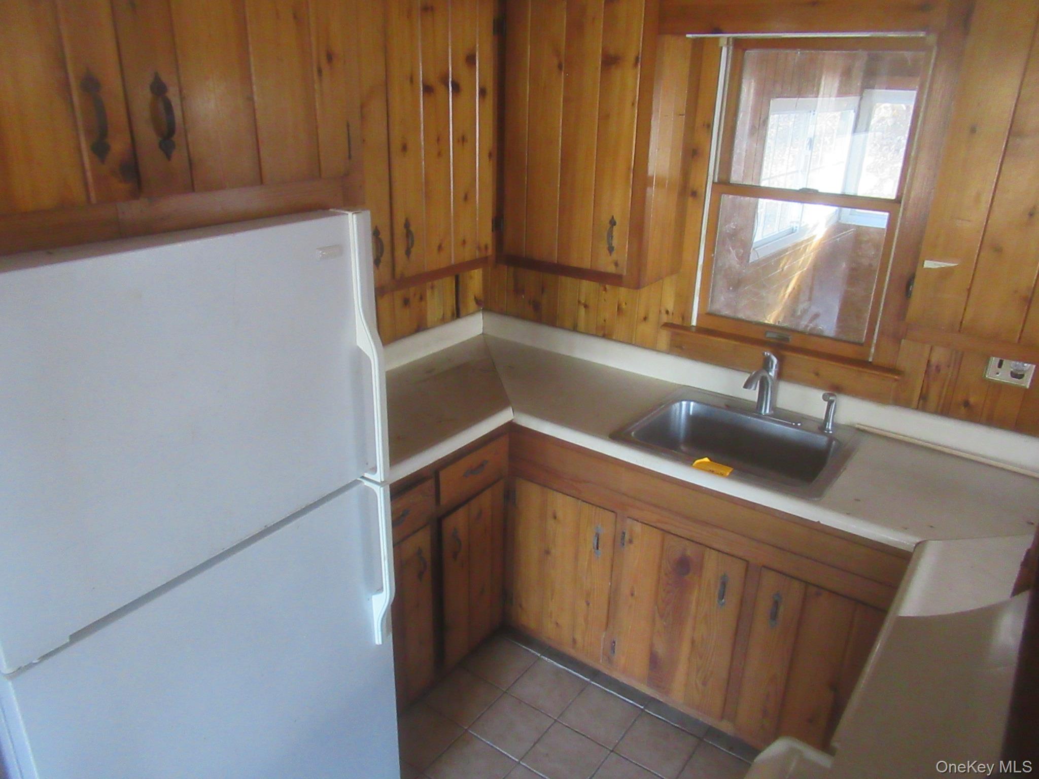 270 Bucks Hollow Road Mahopac, NY 10541 - Photo 4 of 10 Kitchen with freestanding refrigerator, light countertops, brown cabinetry, wooden walls, and light tile patterned floors