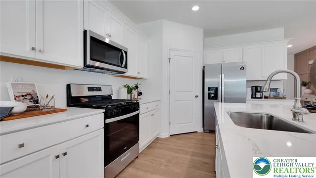 a kitchen with stainless steel appliances a microwave a stove a refrigerator a sink a dining table and chairs with wooden floor