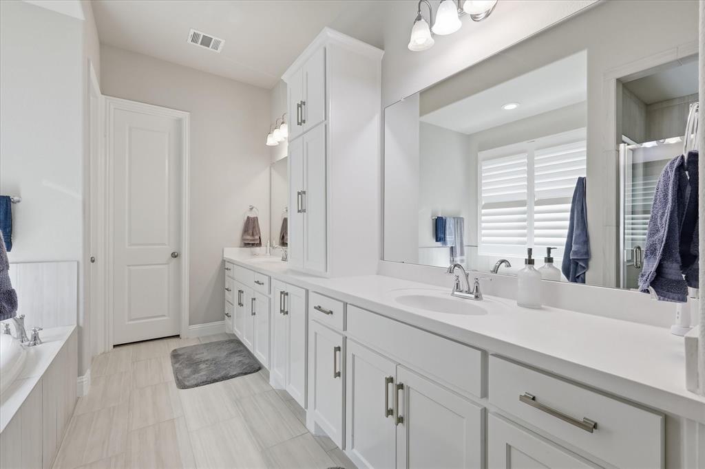 9708 Surveyor Road Oak Point, TX 75068 - Photo 24 of 34 Primary Spacious bathroom featuring a dual vanity with white cabinetry and integrated sinks, extensive countertop space, an oversized mirror, a built-in tub, and light-toned tile flooring