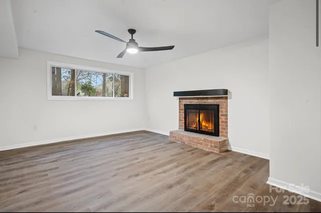 a view of an empty room with wooden floor fireplace and a window