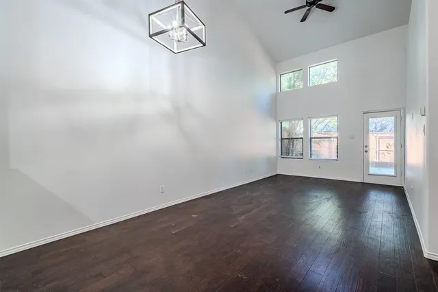 an empty room with wooden floor chandelier fan and windows