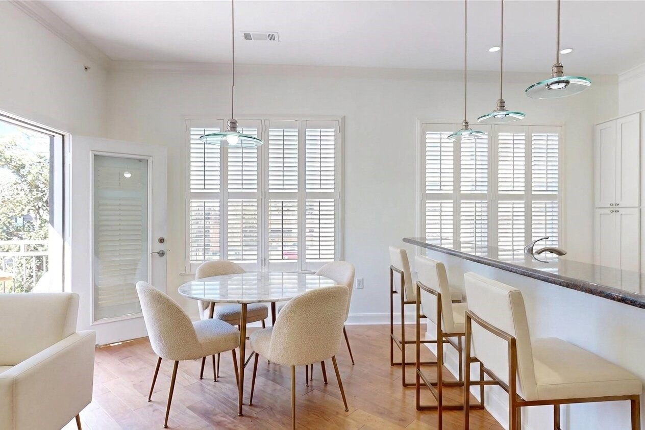 1010 Rosine Street, Unit 29 Houston, TX 77019 - Photo 11 of 16 Bright and airy kitchen with large windows, featuring a cozy dining area, modern pendant lighting, and a breakfast bar with high-back chairs. (Virtual Staging)