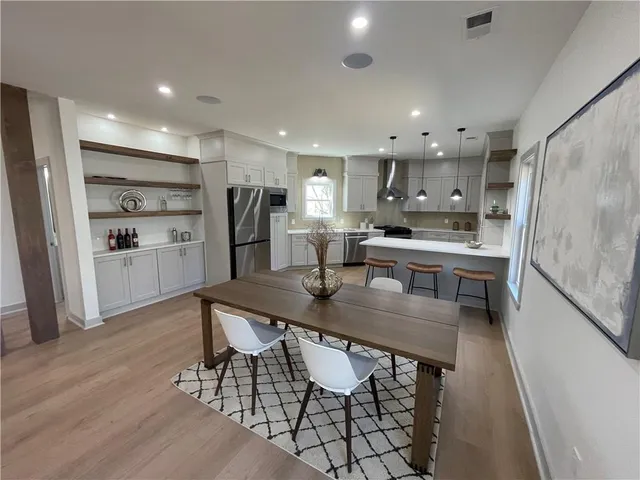 a kitchen with stainless steel appliances kitchen island granite countertop a refrigerator a stove a sink and a dining table with wooden floor