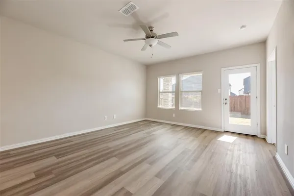 an empty room with wooden floor a ceiling fan and windows