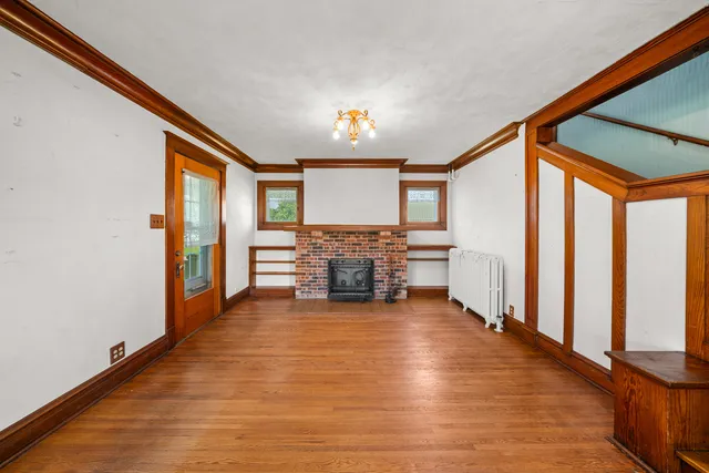 a view of an empty room with wooden floor fireplace and a window