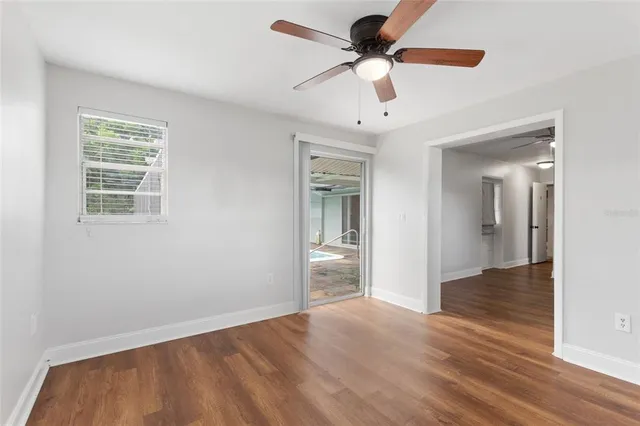 an empty room with wooden floor fan and windows