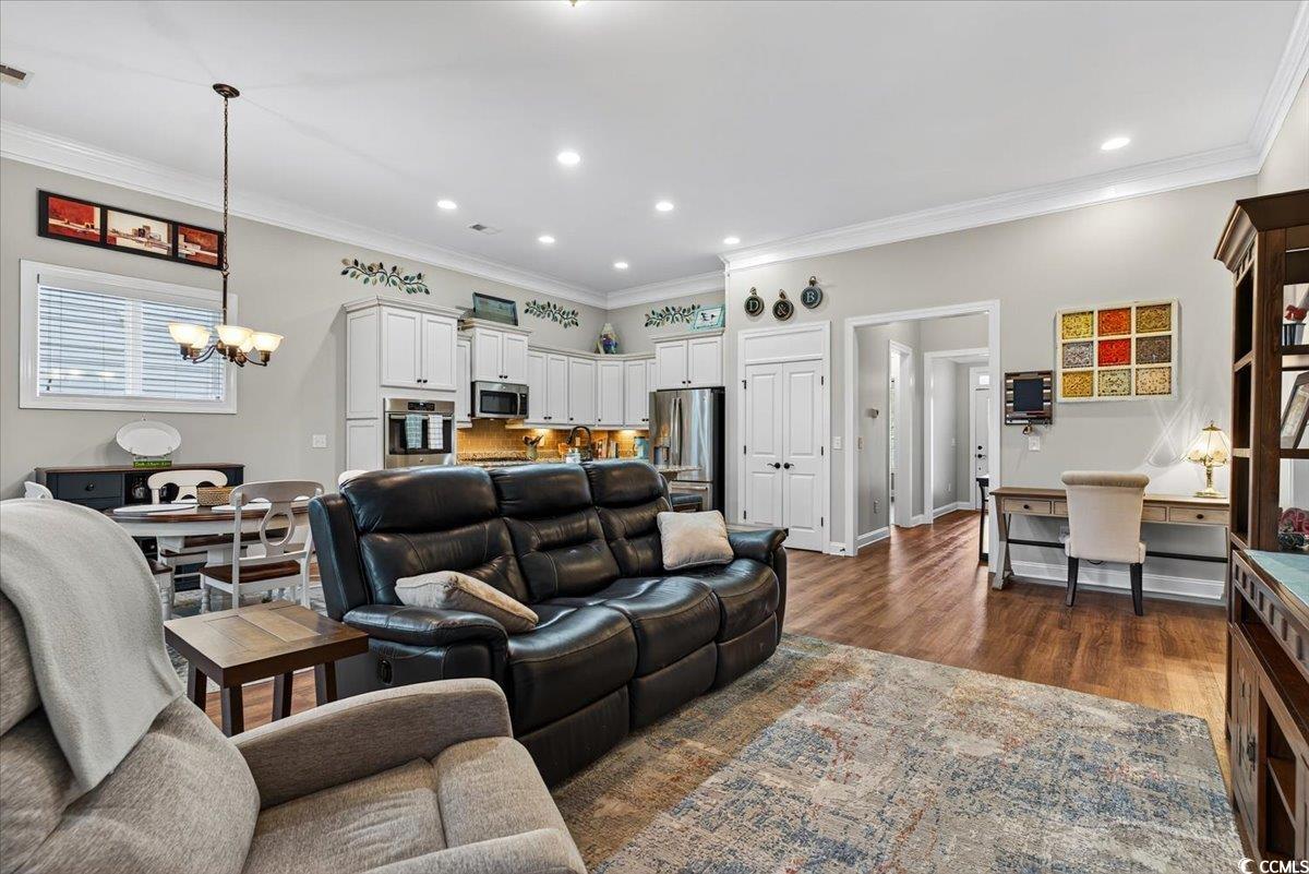 Living area featuring a chandelier, dark wood-style floors, ornamental molding, and recessed lighting