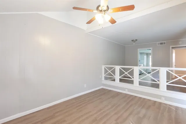 an empty room with wooden floor fan and windows