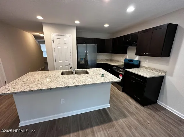 a kitchen with stainless steel appliances kitchen island granite countertop a refrigerator a sink and wooden cabinets