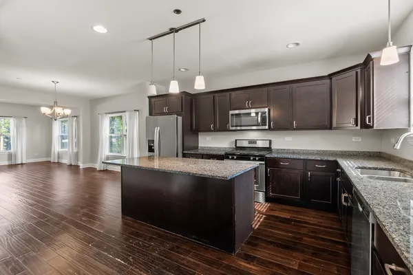 a large kitchen with stainless steel appliances granite countertop a stove a refrigerator a sink dishwasher a oven and a dining table with wooden floor