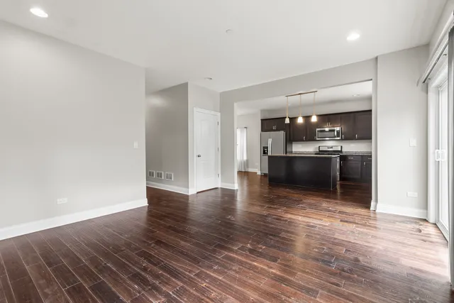 an empty room with wooden floor and kitchen view