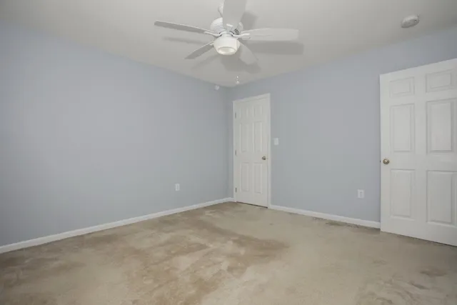 an empty room with a chandelier fan and windows