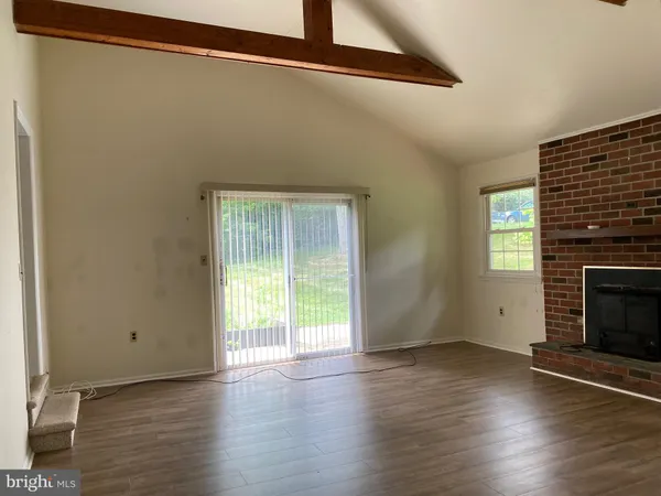 a view of an empty room with wooden floor fireplace and a window