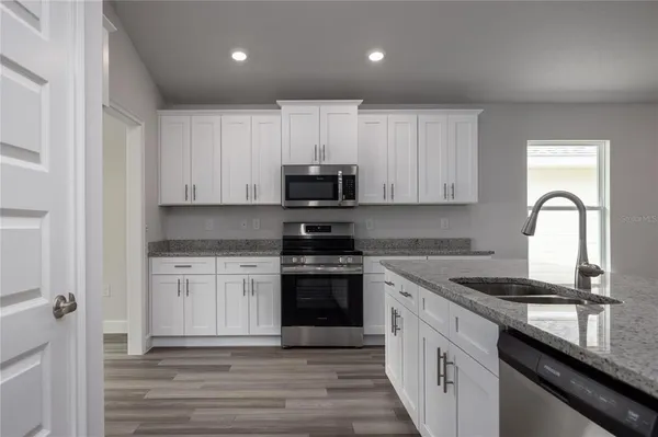 a kitchen with stainless steel appliances granite countertop a sink dishwasher a stove and a refrigerator with wooden floor