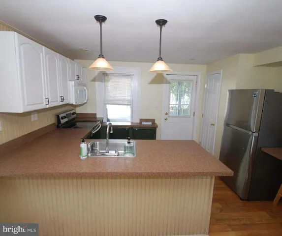 a kitchen with kitchen island a refrigerator a stove a sink dishwasher a dining table and chairs with wooden floor