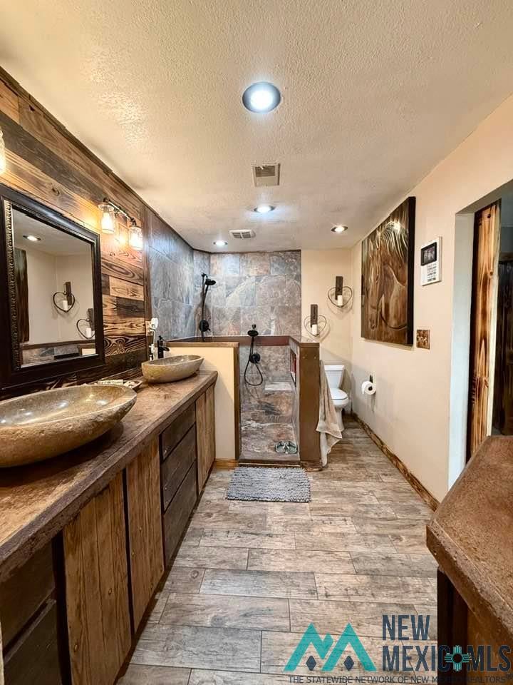 5404 Sioux Road Carlsbad, NM 88220 - Photo 57 of 100 Bathroom featuring dual stone vessel sinks, a wood-finish double vanity with integrated storage, a tiled shower enclosure, and wood-look tile flooring