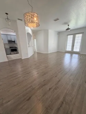 an empty room with wooden floor chandelier and windows