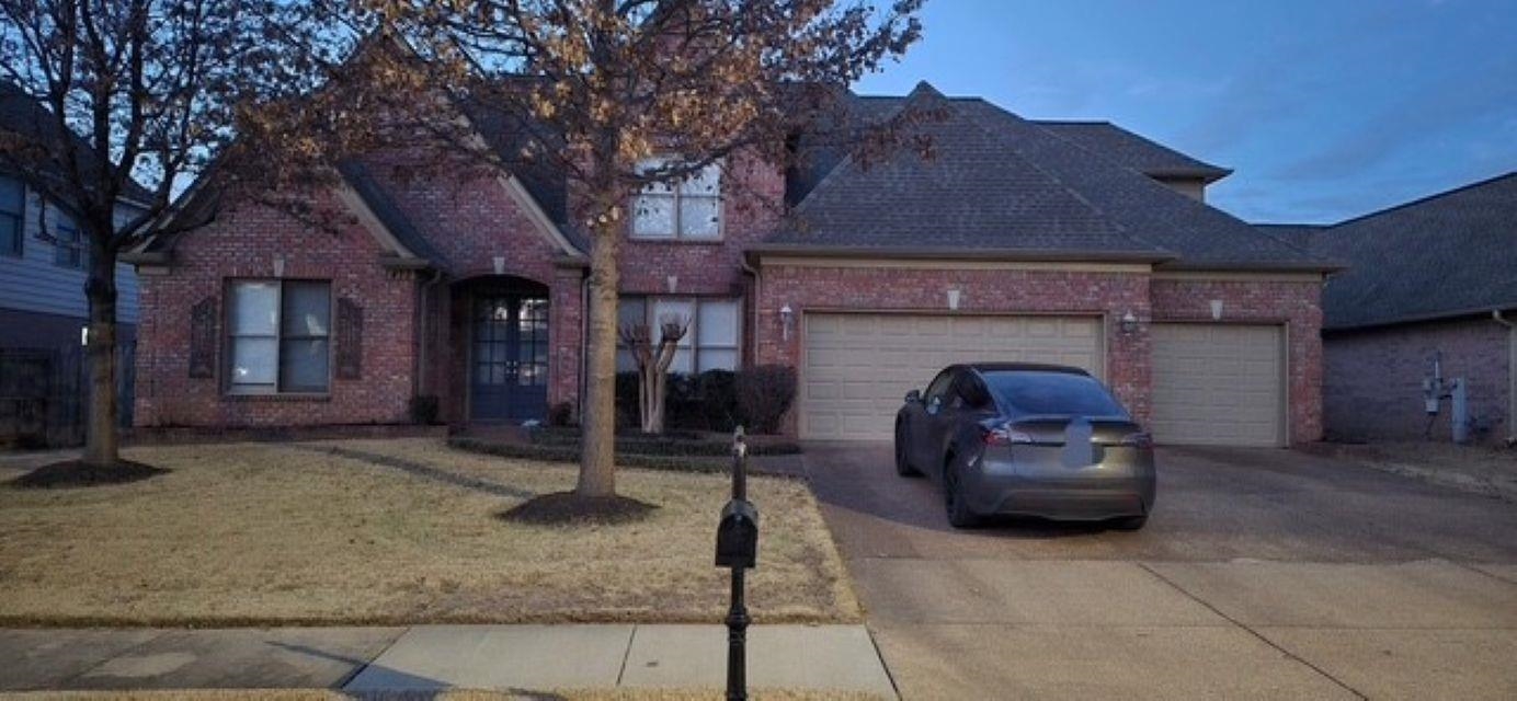 View of front facade featuring driveway, brick siding, a garage, and a front lawn