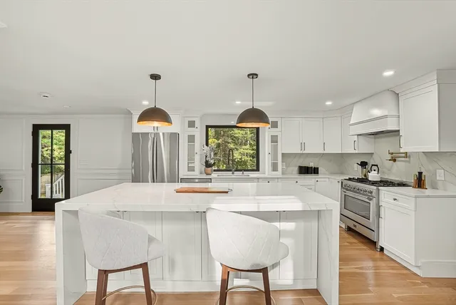 a kitchen with stainless steel appliances kitchen island granite countertop a stove a sink a refrigerator and white cabinets with wooden floor