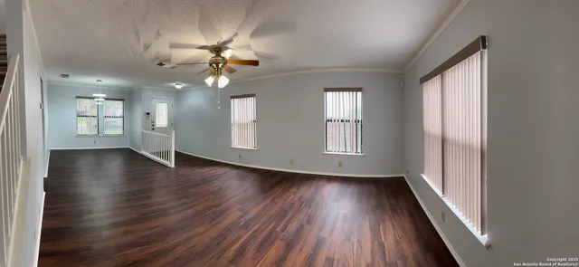 an empty room with wooden floor chandelier fan and windows