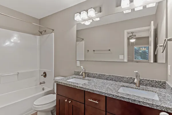 a bathroom with a granite countertop sink a toilet a mirror a bathtub and shower