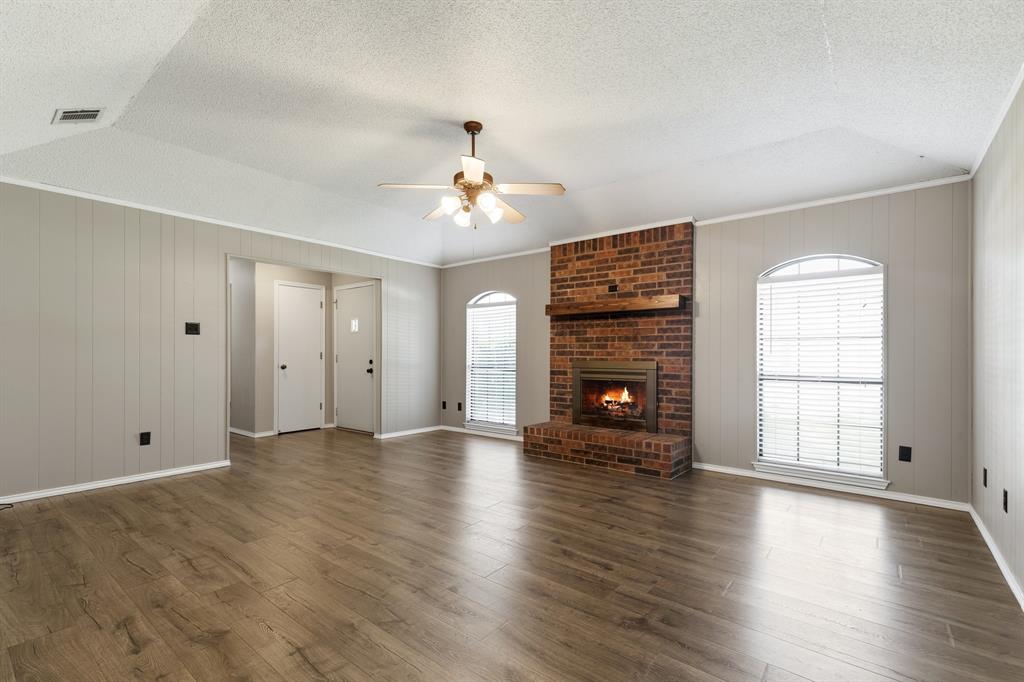 6612 Patsy Lane Watauga, TX 76148 - Photo 7 of 32 Spacious room featuring wood-finish flooring, a brick fireplace with a wood mantel, and two arched windows with blinds