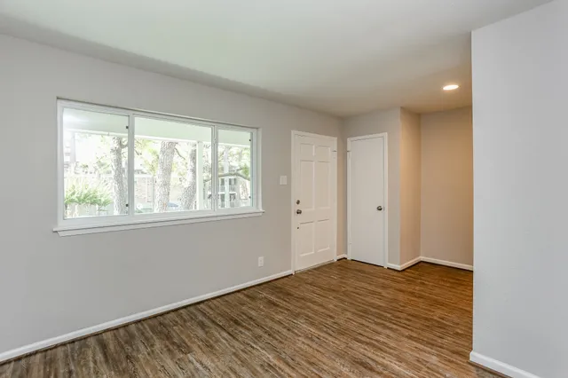 a view of an empty room with wooden floor and a window
