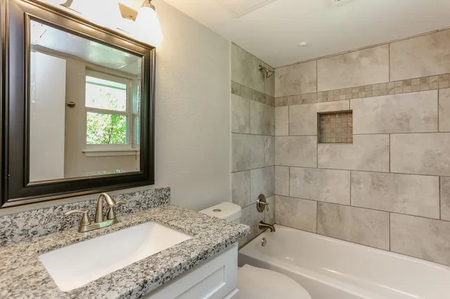 a bathroom with a granite countertop sink a mirror and a bathtub