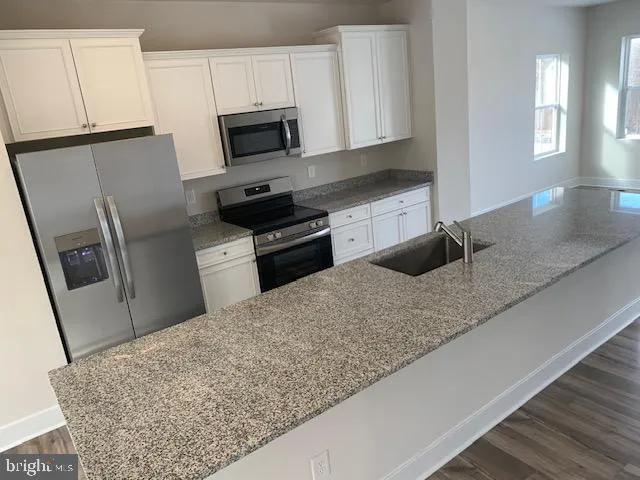 a kitchen with granite countertop a sink a stove top oven a refrigerator and cabinets