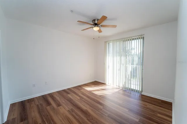 a view of an empty room with wooden floor and a ceiling fan