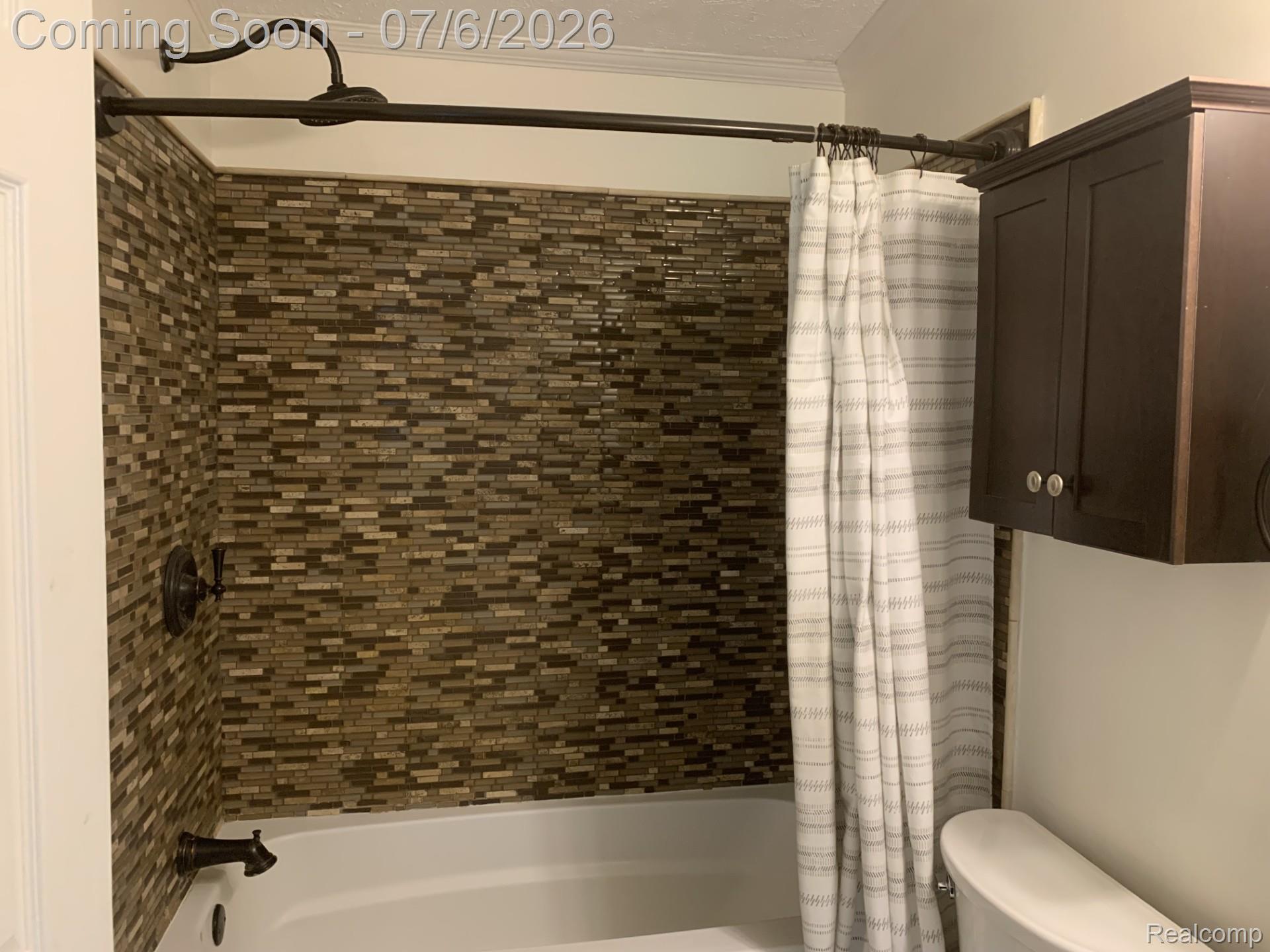 4168 Harris Road Fort Gratiot, MI 48059 - Photo 24 of 30 Bathroom featuring a white bathtub, mosaic-tiled shower surround, dark bronze fixtures, and a wall-mounted storage cabinet