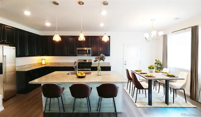 a kitchen with stainless steel appliances kitchen island granite countertop a dining table chairs and a refrigerator