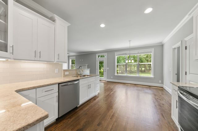 a kitchen with stainless steel appliances granite countertop a stove a sink and white cabinets with wooden floor next to windows