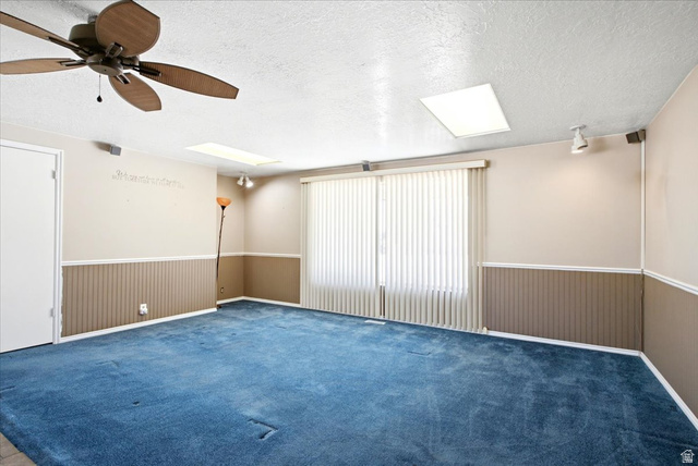7050 South 260 East Midvale, UT 84047 - Photo 8 of 28 Spacious room featuring a ceiling fan, two skylights, and vertical blinds over a large window