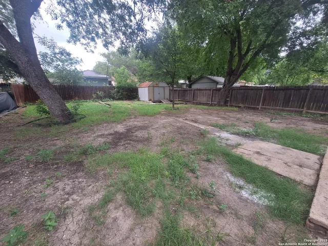 a view of a backyard with large trees and wooden fence