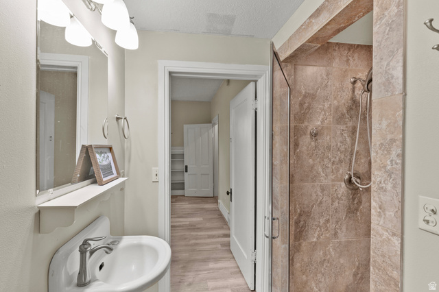 148 South 300 East Logan, UT 84321 - Photo 11 of 29 Bathroom featuring a pedestal sink with a chrome faucet, a vanity mirror with overhead four-bulb light fixture, a tiled shower with glass enclosure, and light wood-finish flooring