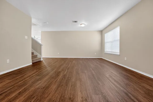 a view of an empty room with wooden floor and window