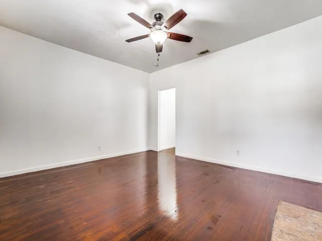an empty room with wooden floor and a ceiling fan