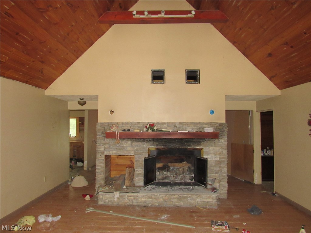 5575 Center Road Conneaut, OH 44030 - Photo 5 of 19 Vaulted wood-paneled ceiling with exposed beams, central stone-clad fireplace with mantel, and wood-finish flooring