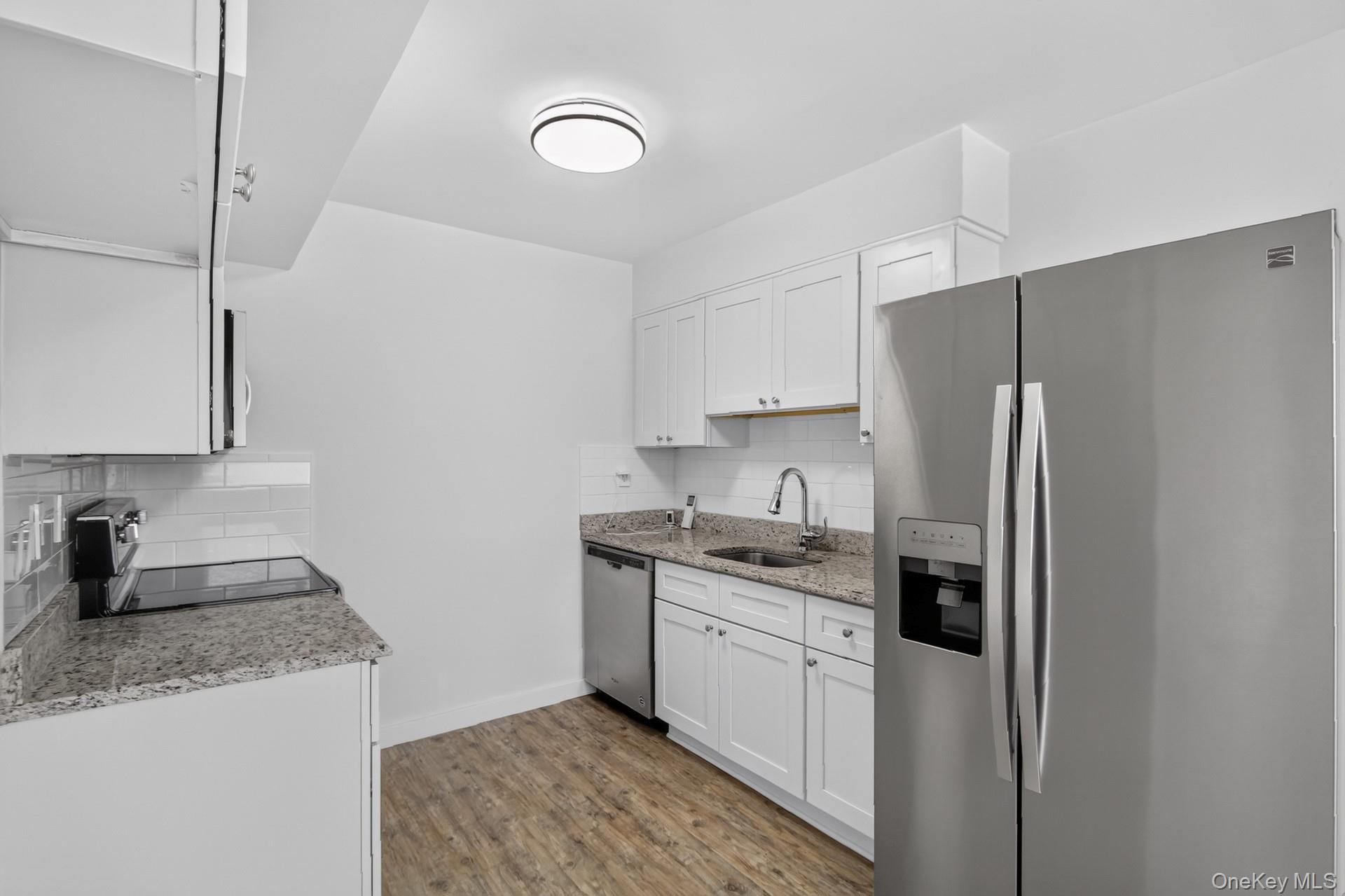 26 Cooper Road, Unit 414 Poughkeepsie, NY 12603 - Photo 13 of 24 Updated kitchen featuring white shaker cabinetry, granite countertops, subway tile backsplash, stainless steel appliances, and wood-finish flooring
