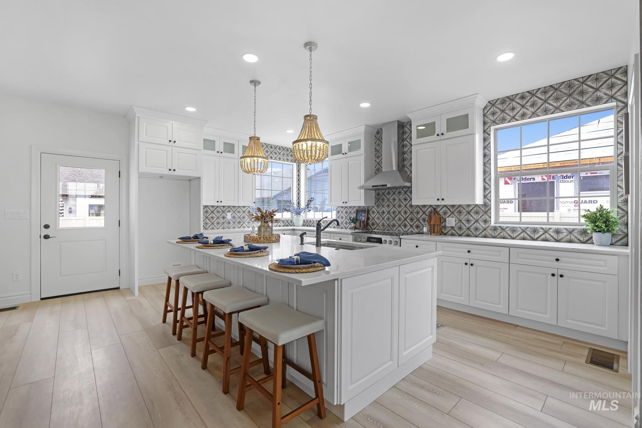 866 Quartz Road Kimberly, ID 83341 - Photo 13 of 48 Bright kitchen featuring a large central island with seating, white shaker cabinetry, quartz countertops, a decorative tile backsplash, and wood-finish flooring