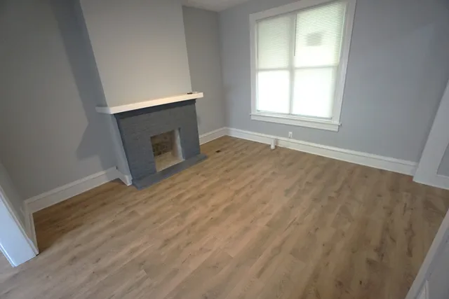 an empty room with wooden floor fireplace and windows