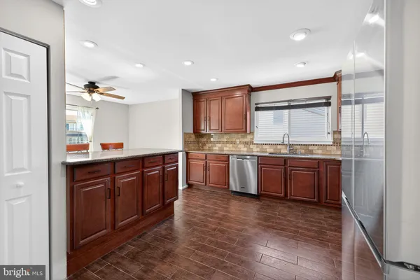 a room with kitchen island granite countertop wooden floors stainless steel appliances a sink and a window