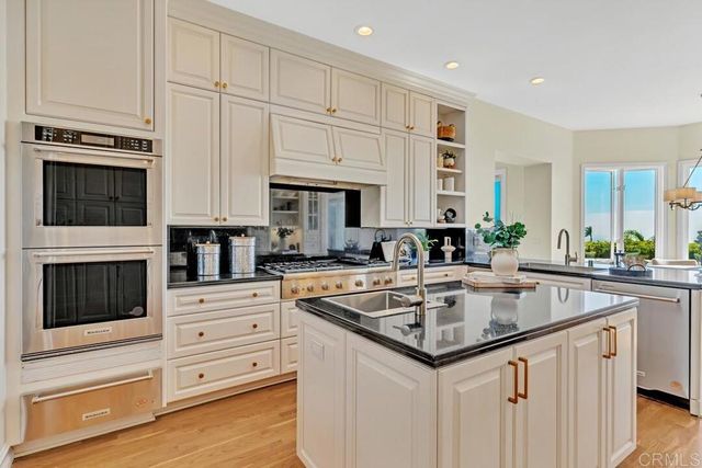 a kitchen with stainless steel appliances granite countertop a stove a sink dishwasher and white cabinets with wooden floor