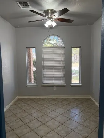 an empty room that has a window and a chandelier fan