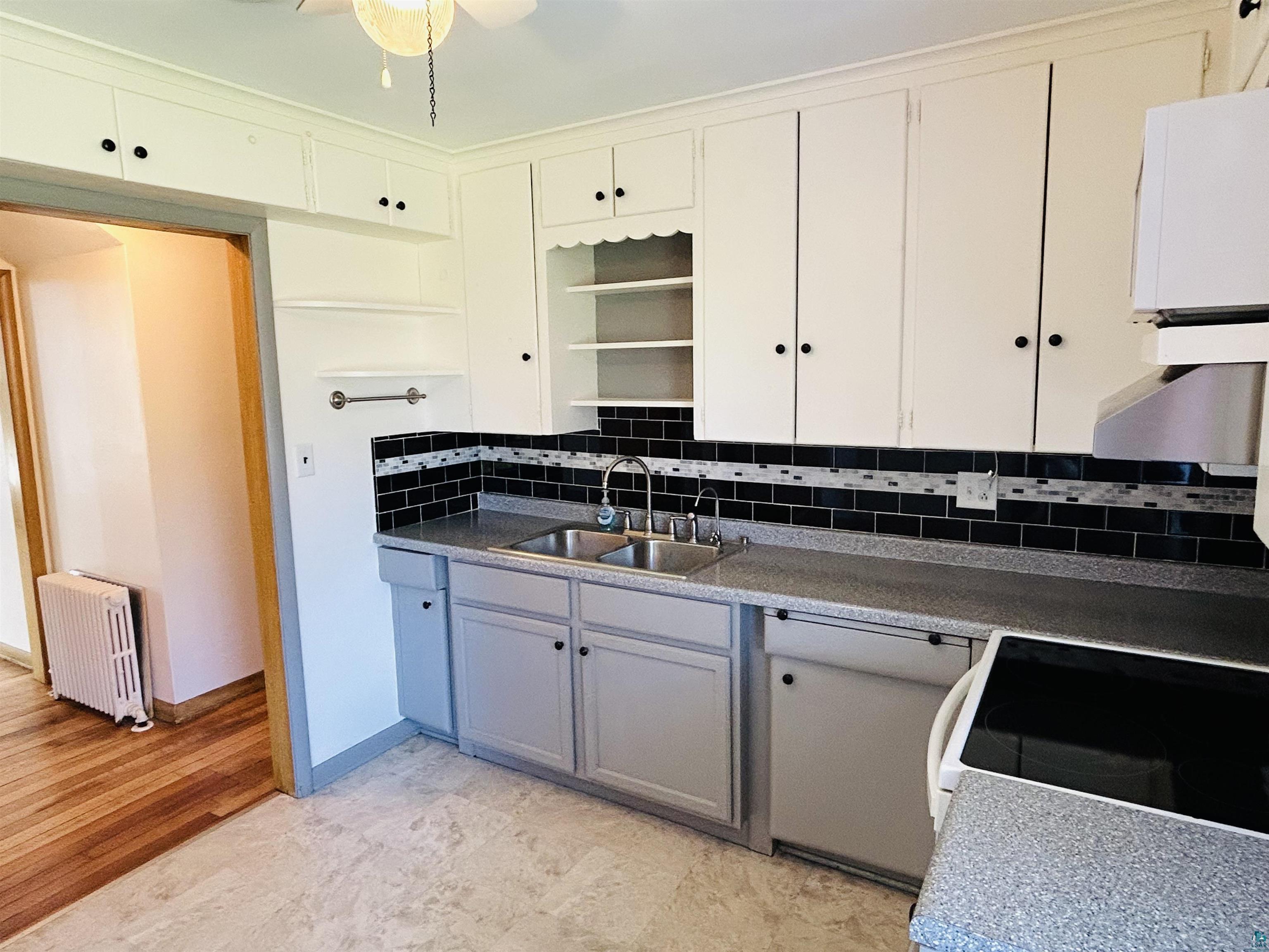 5090 London Road, Unit 1 Duluth, MN 55804 - Photo 11 of 54 Kitchen featuring abundant white cabinetry, dark subway tile backsplash with accent mosaic, double basin sink, and wood-finish flooring in the adjacent room