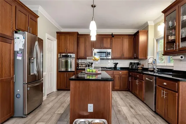 a kitchen with stainless steel appliances granite countertop a refrigerator a sink dishwasher a stove and a dining table with wooden floor