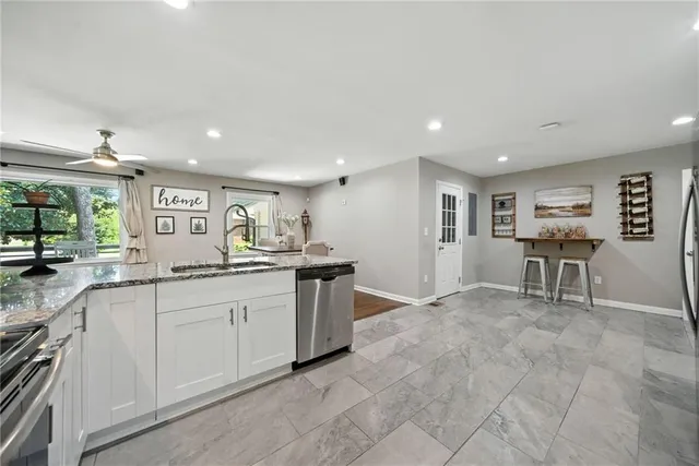 a large white kitchen with granite countertop a sink and chairs