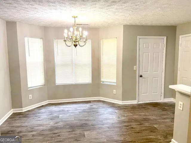 an empty room with wooden floor chandelier and windows