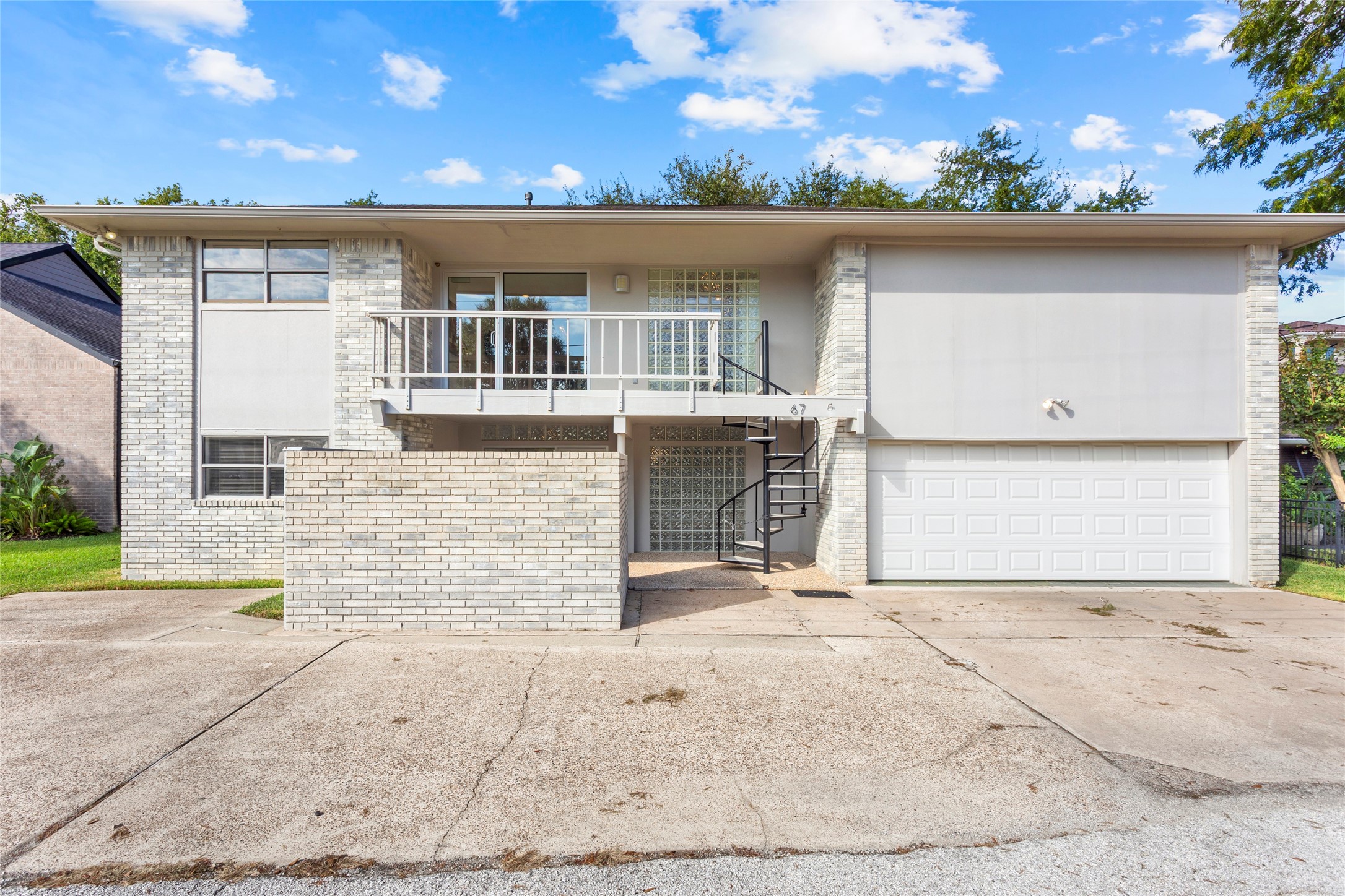 67 Harbor Lane Kemah, TX 77565 - Photo 41 of 47 This modern two-story home features a light brick exterior with large windows for natural light. It includes a spacious two-car garage and a distinctive spiral staircase leading to the upper level. The driveway offers ample parking space, and the surrounding lawn is well-maintained.